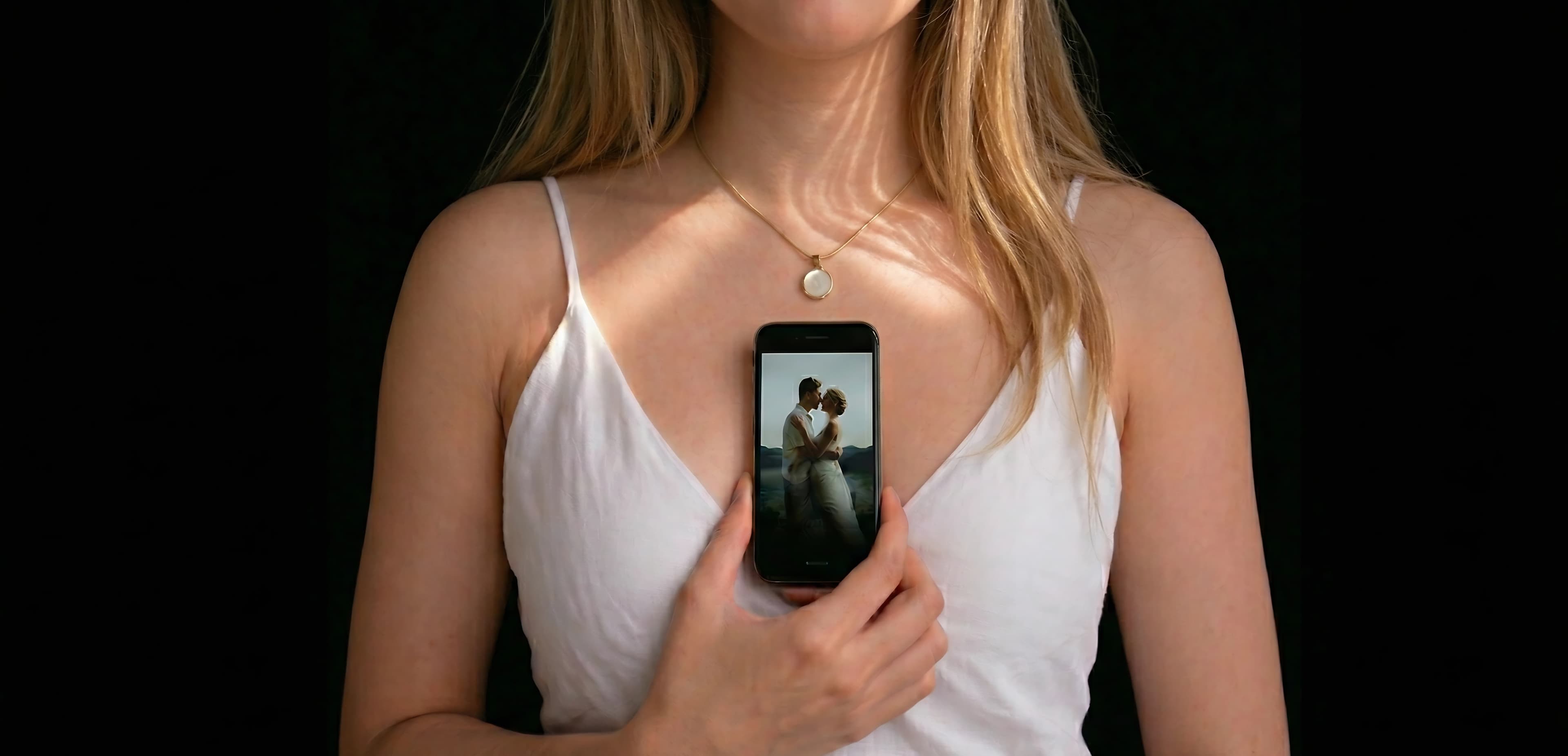 A gold Memoura pendant necklace with a phone displaying a cherished memory