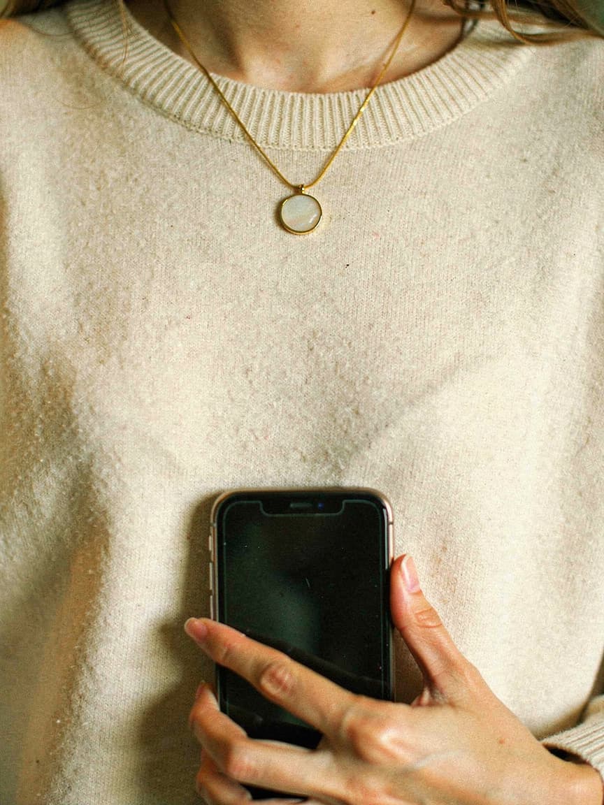 A hand holding a phone to a round mother-of-pearl Memoura pendant