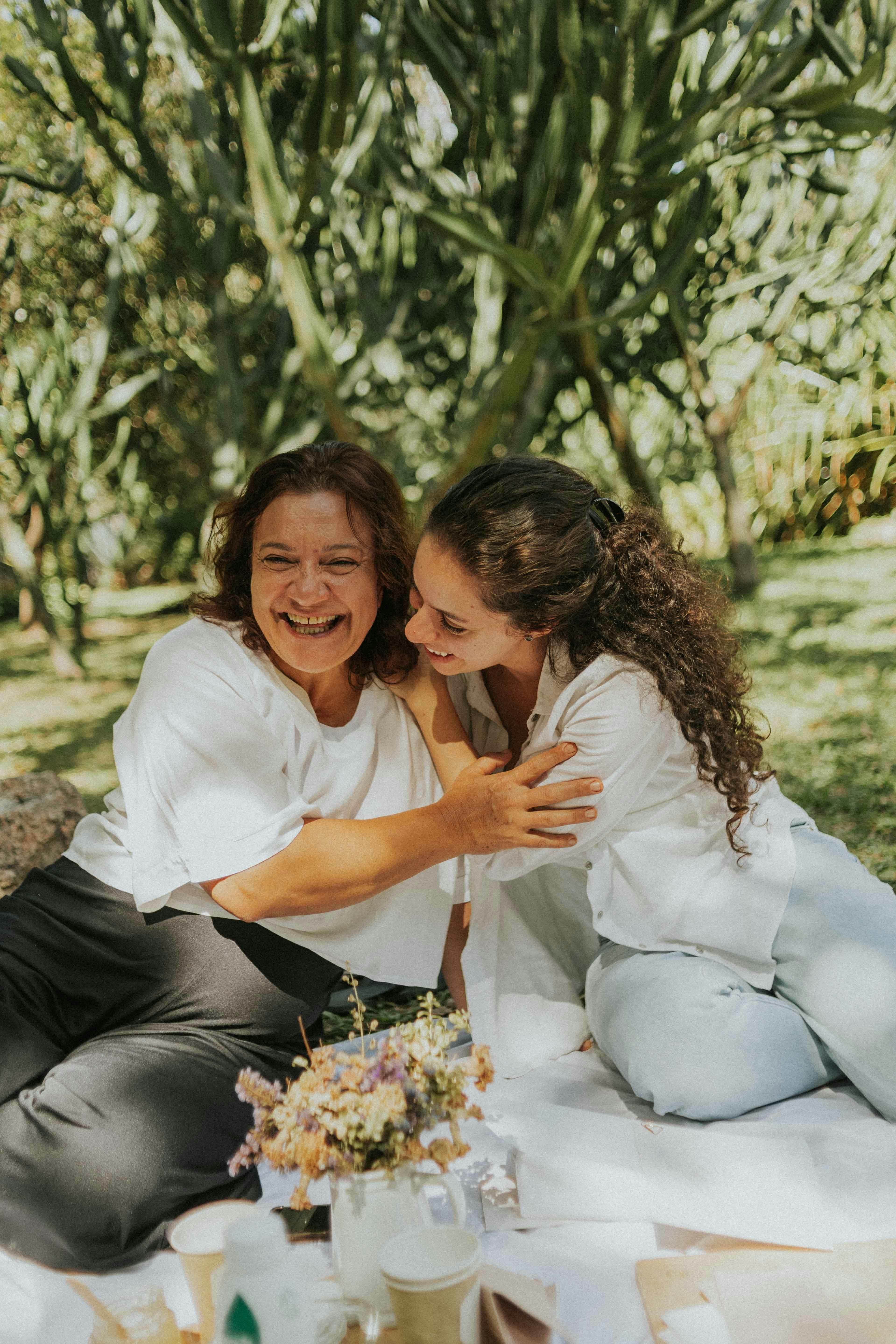A mother and her adult daughter laughing together over coffee, warm kitchen light, close and candid
